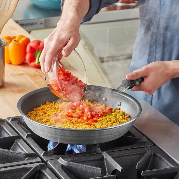 A person pouring chopped red bell peppers into a Vollrath Wear-Ever non-stick fry pan on a stove.