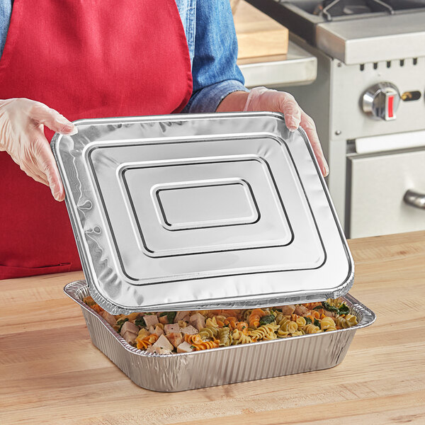A woman holding a Western Plastics foil tray with food in it.