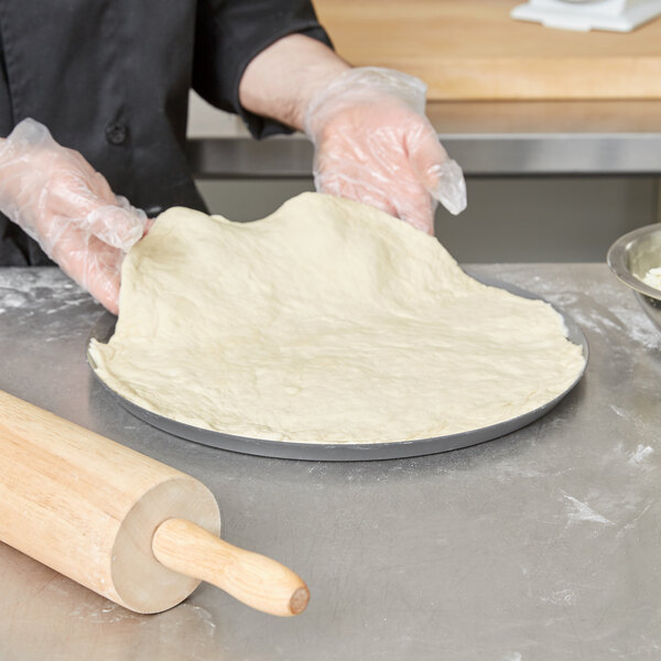 A person in gloves using a rolling pin to roll out pizza dough on an American Metalcraft Super Perforated Pizza Pan.