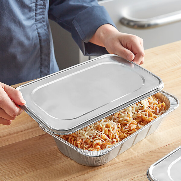 A person holding a Western Plastics foil steam table pan lid over a tray of food.