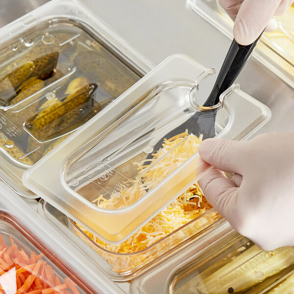 A gloved hand using a knife to cut food in a plastic container with a clear plastic lid.