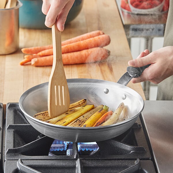 A person cooking grilled vegetables in a Vollrath Wear-Ever aluminum fry pan on a stove.
