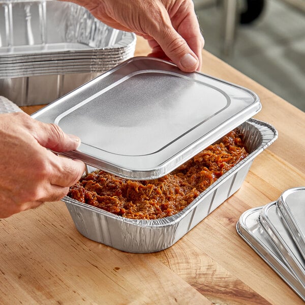 A person's hand opening a Western Plastics foil pan filled with food.