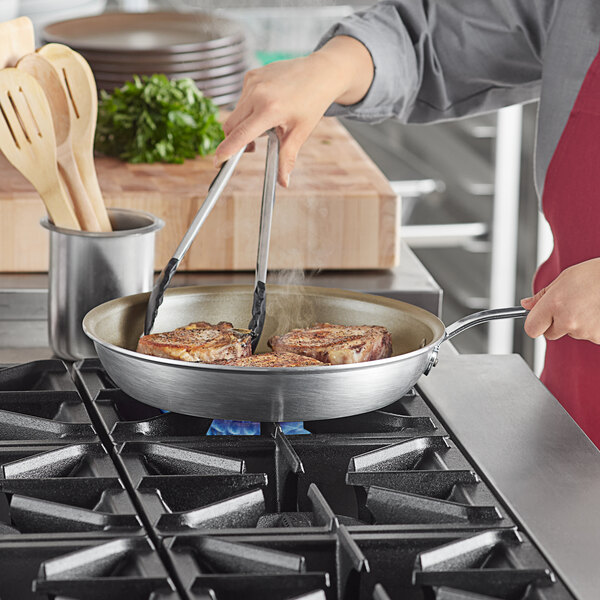 A person cooking meat in a Vollrath Wear-Ever aluminum non-stick fry pan with a metal handle.