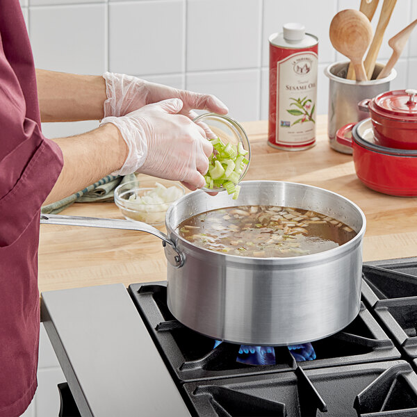 A person cooking soup in a Vollrath Wear-Ever sauce pan on a stove.