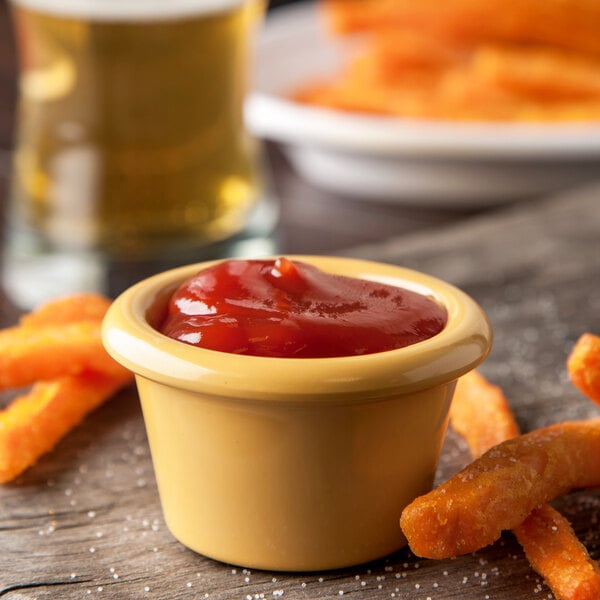 A Carlisle honey yellow ramekin filled with ketchup on a table with french fries.