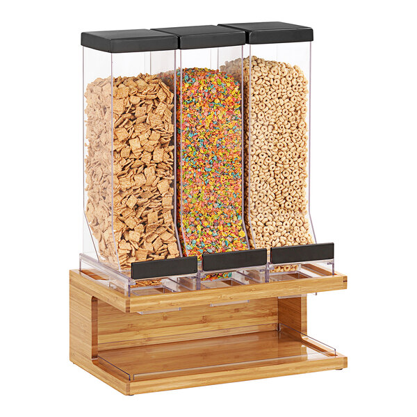 A Cal-Mil Bamboo wood triple canister cereal dispenser holding a variety of cereals.