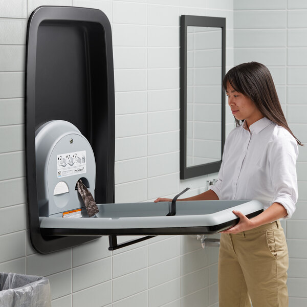 A woman holding a Koala Kare stainless steel vertical baby changing station.