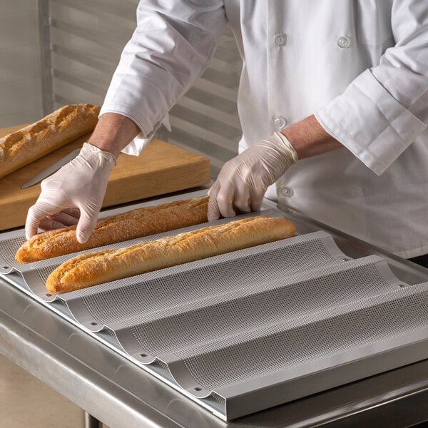 A person in white gloves placing baguettes on a Chicago Metallic French bread pan.