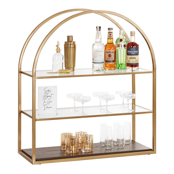 A Cal-Mil gold metal and oak wood 3-tier display shelf with bottles and glasses on it.