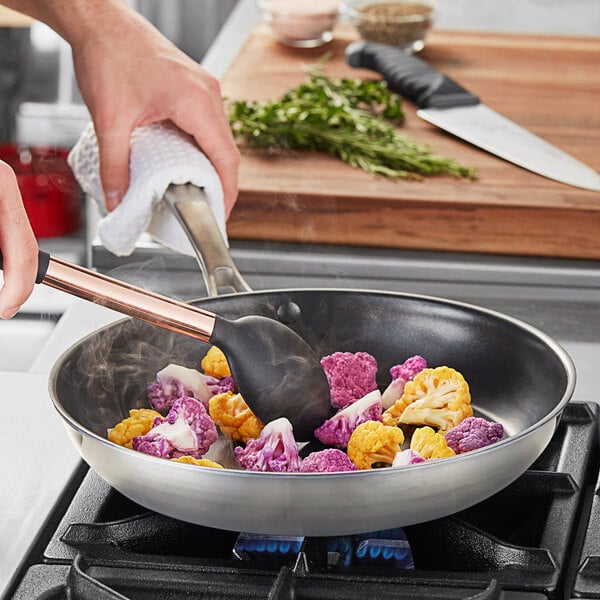 A person cooking yellow and purple cauliflower in a Vigor stainless steel non-stick fry pan.