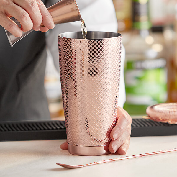 A person pouring a drink into a copper Barfly cocktail shaker.