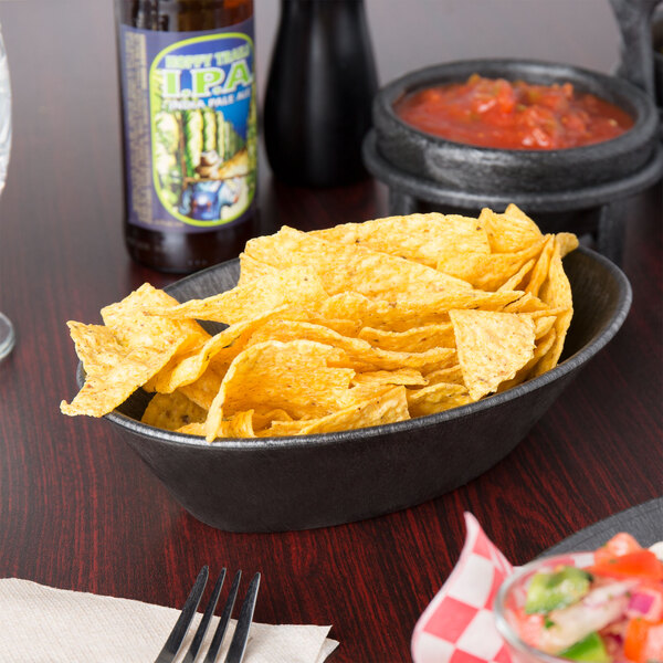 A charcoal polyethylene oval basket filled with chips on a table with salsa.