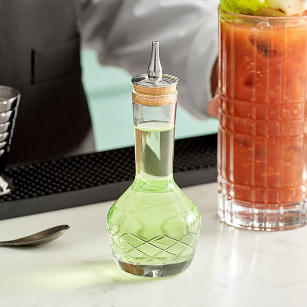 A bartender pours green liquid from a Barfly glass bitters bottle into a glass.