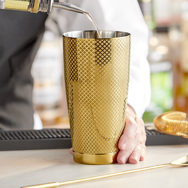 A bartender using a Barfly gold cocktail shaker to pour a drink into a gold cup.