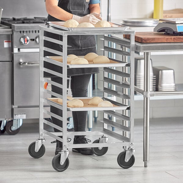 A woman in a professional kitchen using a Regency sheet pan rack to hold trays of dough.