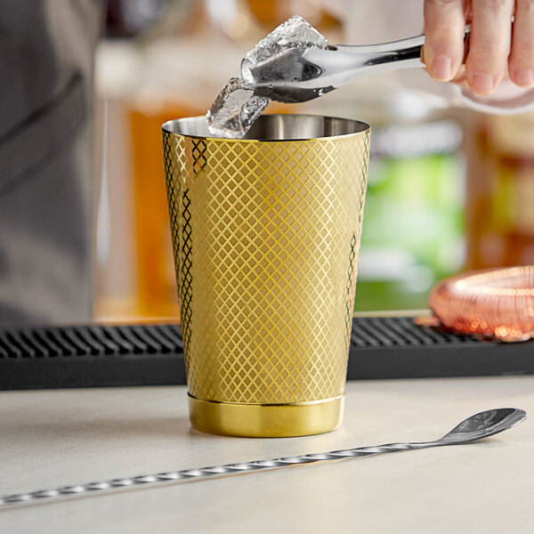 A bartender using a Barfly gold diamond lattice cocktail shaker to pour a drink.