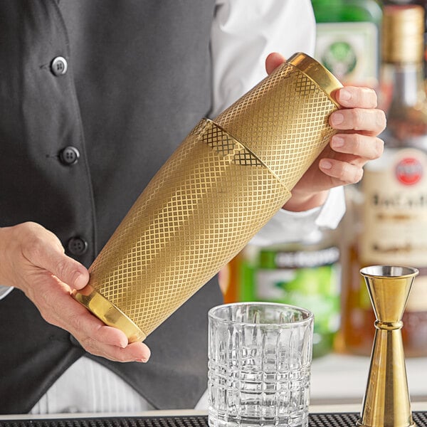A bartender holding a gold Barfly cocktail shaker.