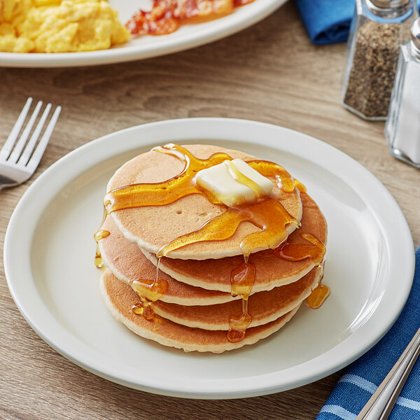 A stack of Krusteaz whole grain pancakes with butter and syrup on a plate.