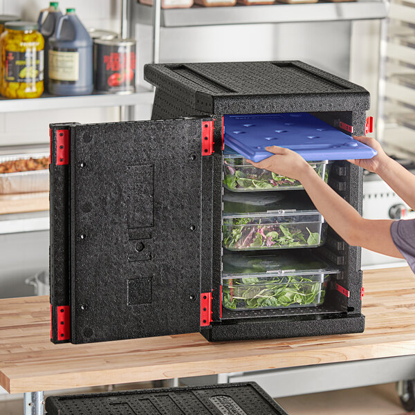 A woman using a CaterGator Dash food pan carrier to store food in a black refrigerator.