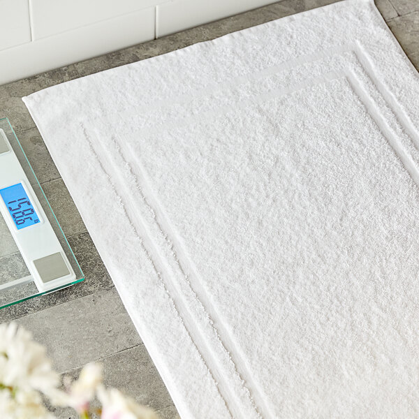 A white Lavex Luxury 100% combed ring-spun cotton bath mat on a grey tile floor next to a digital scale.