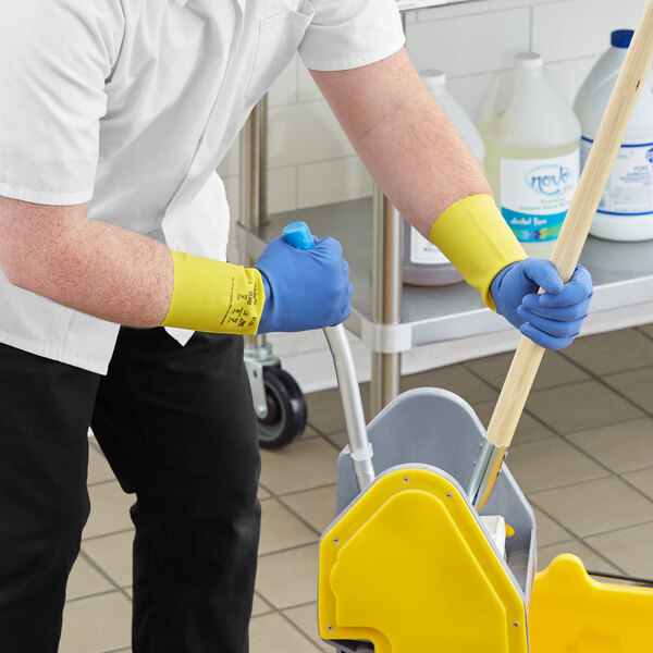 A person wearing blue and yellow Ansell AlphaTec gloves mopping a floor.