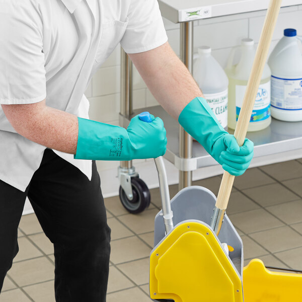 A person wearing green Ansell AlphaTec dishwashing gloves and holding a mop.