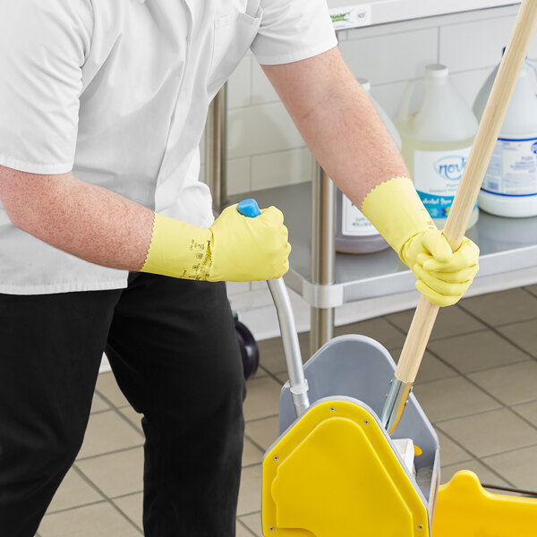 A man wearing yellow Ansell janitorial gloves and holding a mop.