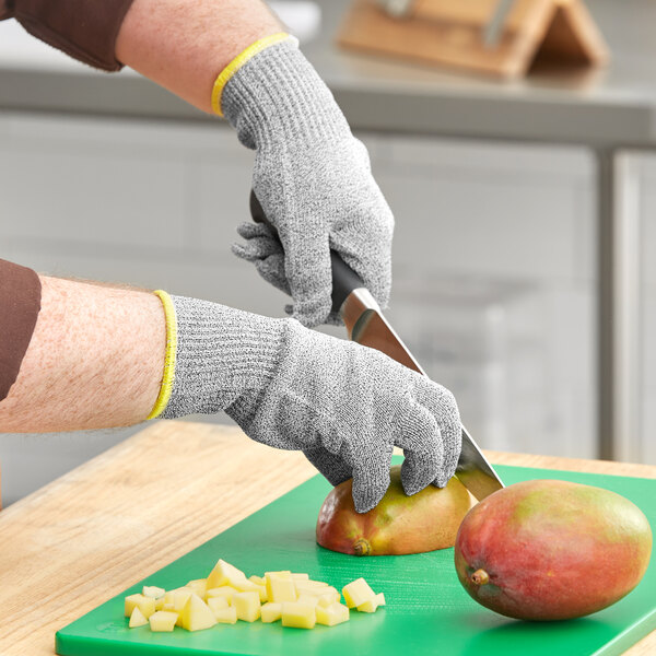 A person wearing Ansell HyFlex cut-resistant gloves cuts a mango on a cutting board.