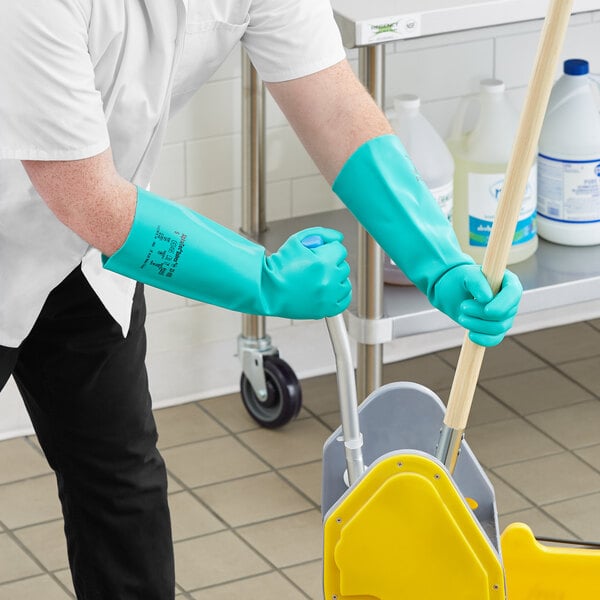 A person wearing green Ansell Solvex gloves and holding a mop.