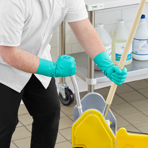 A person wearing green Ansell dishwashing gloves cleaning a mop.