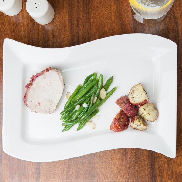 A CAC rectangular porcelain platter with meat, potatoes and green beans on a table.