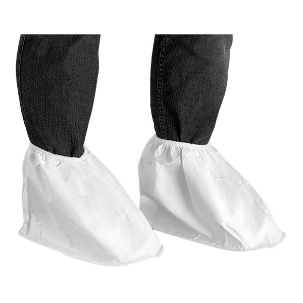 A person wearing Ansell AlphaTec white shoe covers over shoes on their legs.