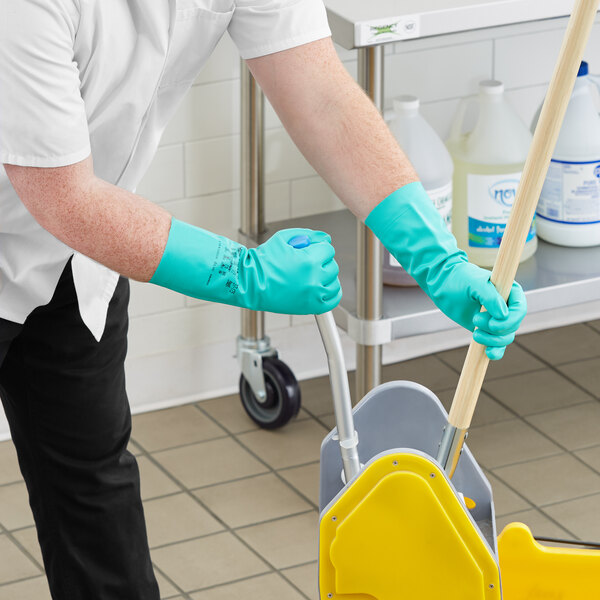 A man wearing green Ansell Solvex gloves and holding a mop cleans a floor.