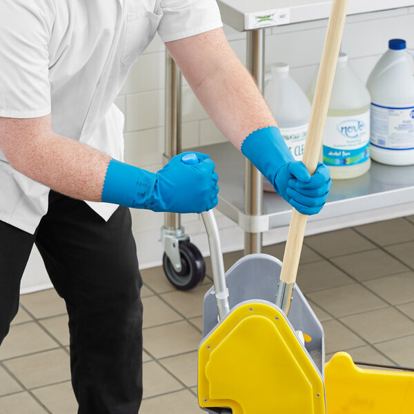 A man wearing blue Ansell AlphaTec dishwashing gloves and holding a mop.