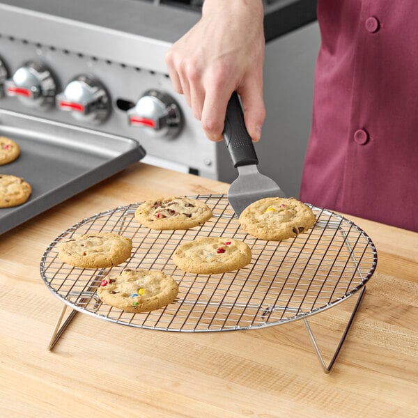 A person using a spatula to place a cookie on a Choice round footed cooling rack.