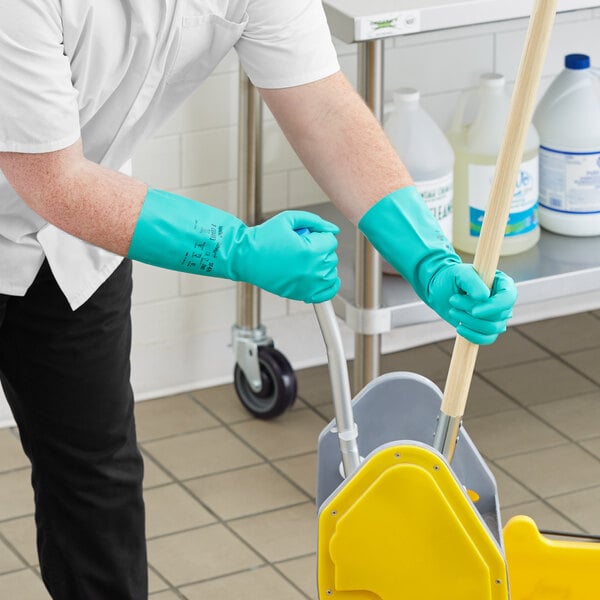 A person wearing green Ansell AlphaTec Solvex gloves mopping the floor in a school kitchen.