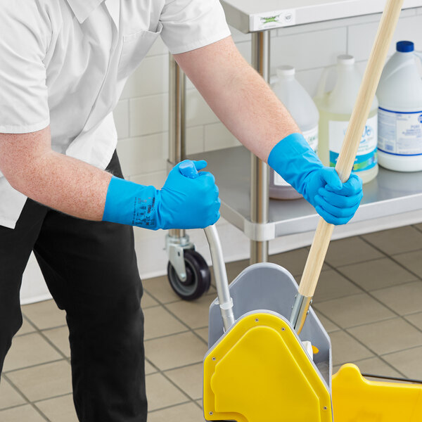A person wearing Ansell blue dishwashing gloves uses a mop to clean a floor.