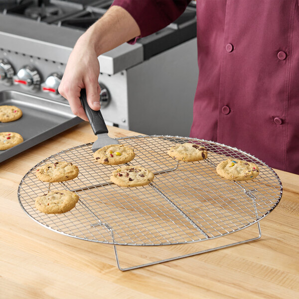 A person holding a spatula over a Choice round chrome cooling rack with cookies.