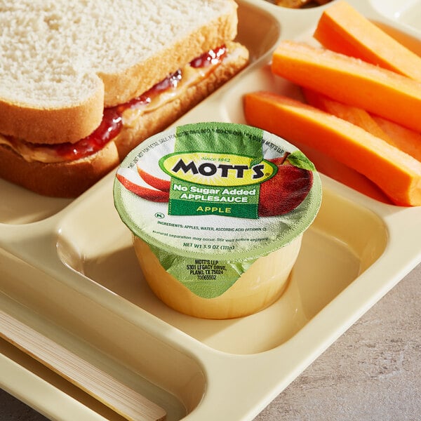 A table with a tray of food including a Mott's No Sugar Added Applesauce cup, sandwich, and fruit.