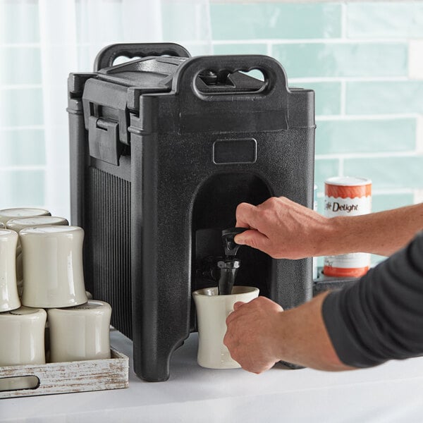 A person pouring coffee from a white insulated beverage dispenser.