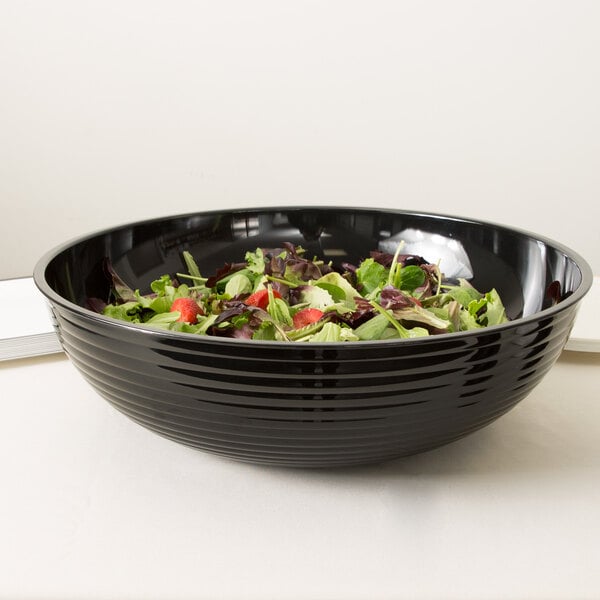 A black Cambro Camwear round ribbed bowl filled with salad on a white table.