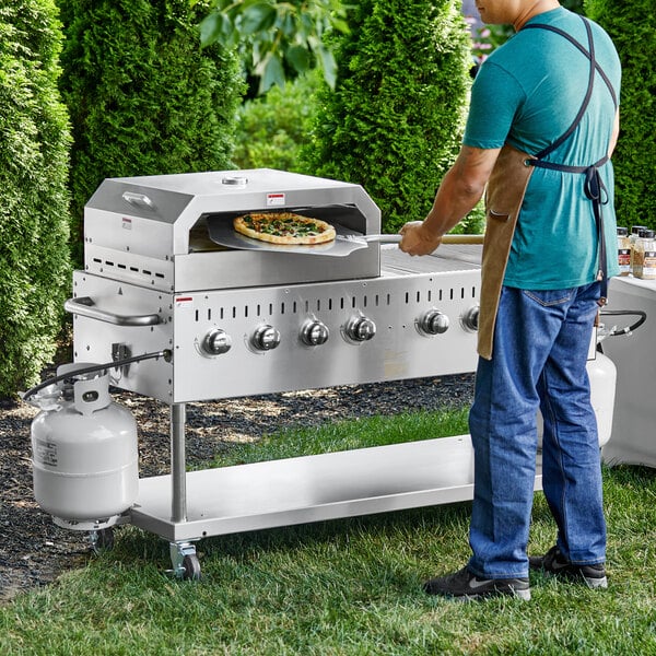 A man cooking a pizza on a Backyard Pro stainless steel grill.