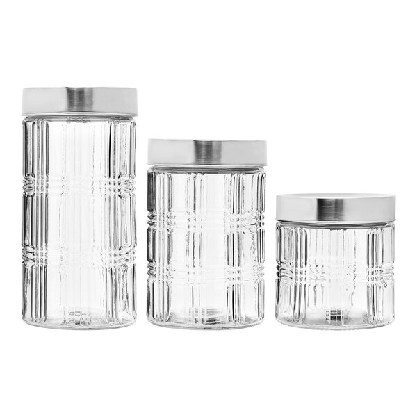 A group of clear glass canisters with silver lids.