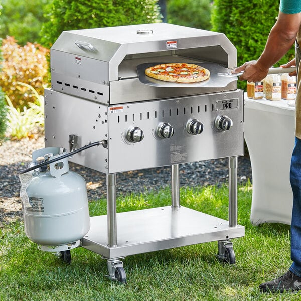 A man using a Backyard Pro stainless steel grill to cook a pizza outdoors.