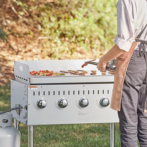 A man using a Backyard Pro stainless steel outdoor grill to cook bacon and peppers.