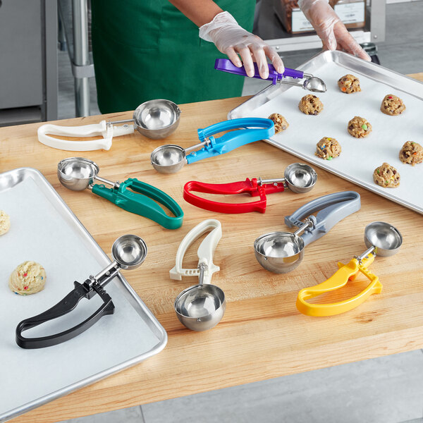 A woman using a Choice EZ Grip Squeeze Handle disher to scoop cookie dough onto a tray of cookies.