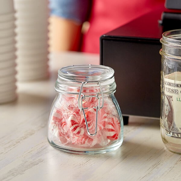 A Choice glass storage jar filled with candy on a table with a dollar bill in it.