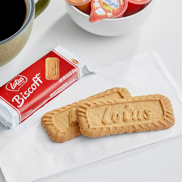 A Lotus Biscoff cookie next to a cup of coffee on a napkin.