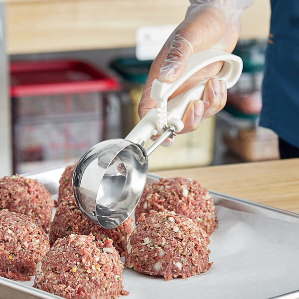 A hand using a white Choice EZ Grip metal scoop to serve meatballs.